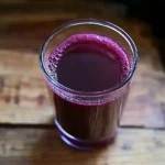 glass of dark purple grape juice on a wooden surface.