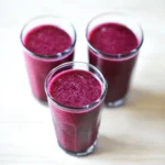 Homemade blueberry juice in clear glasses on a light wooden surface
