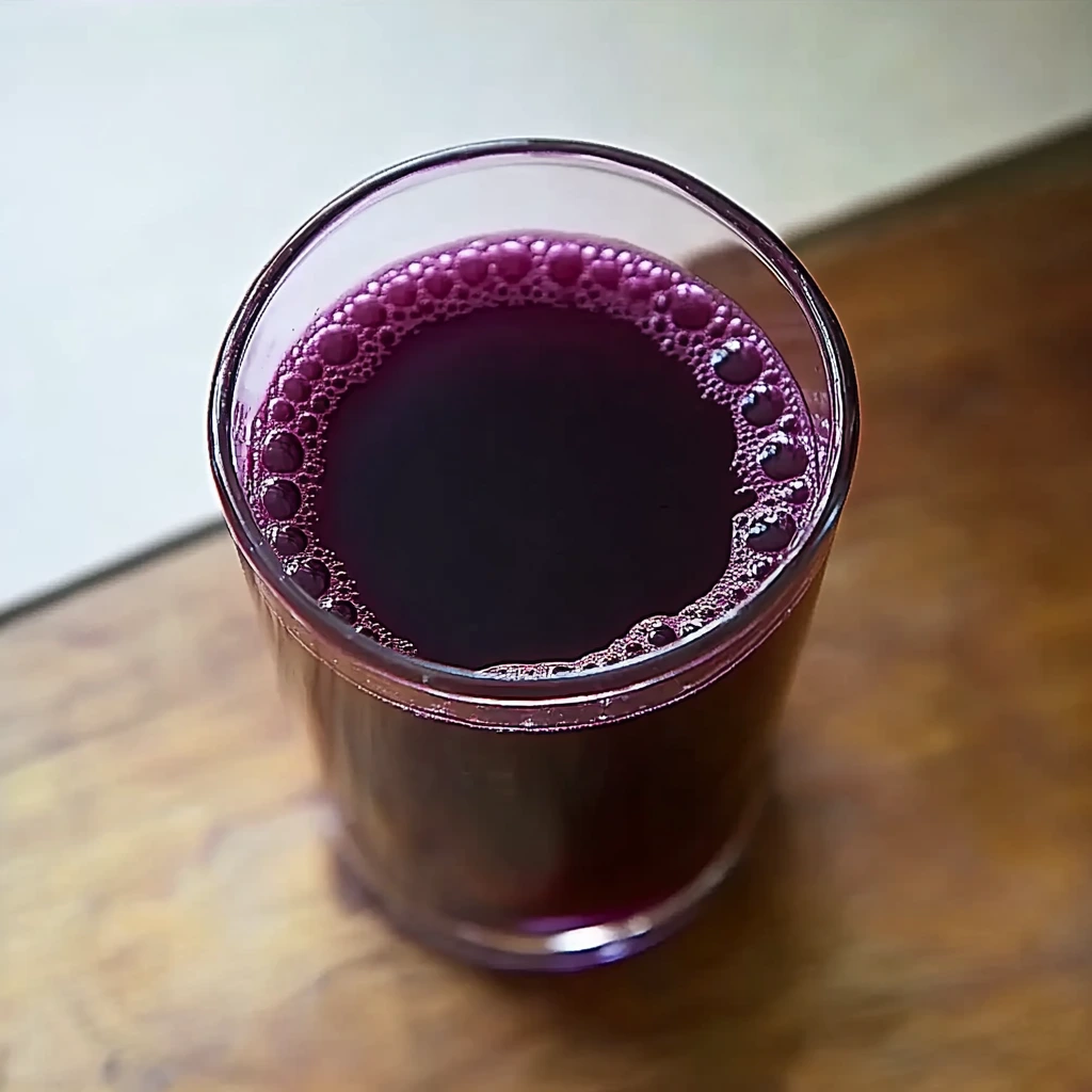 glass of dark purple grape juice on a wooden surface.