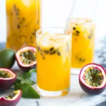 Fresh passion fruit juice with ice and mint in a glass, surrounded by ripe passion fruits